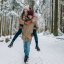 Mann trägt seine Frau beim Spazieren durch verschneiten Bayerischen Wald